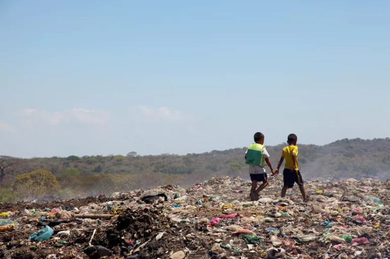 A photograph of two children from behind, walking on a pile of garbage