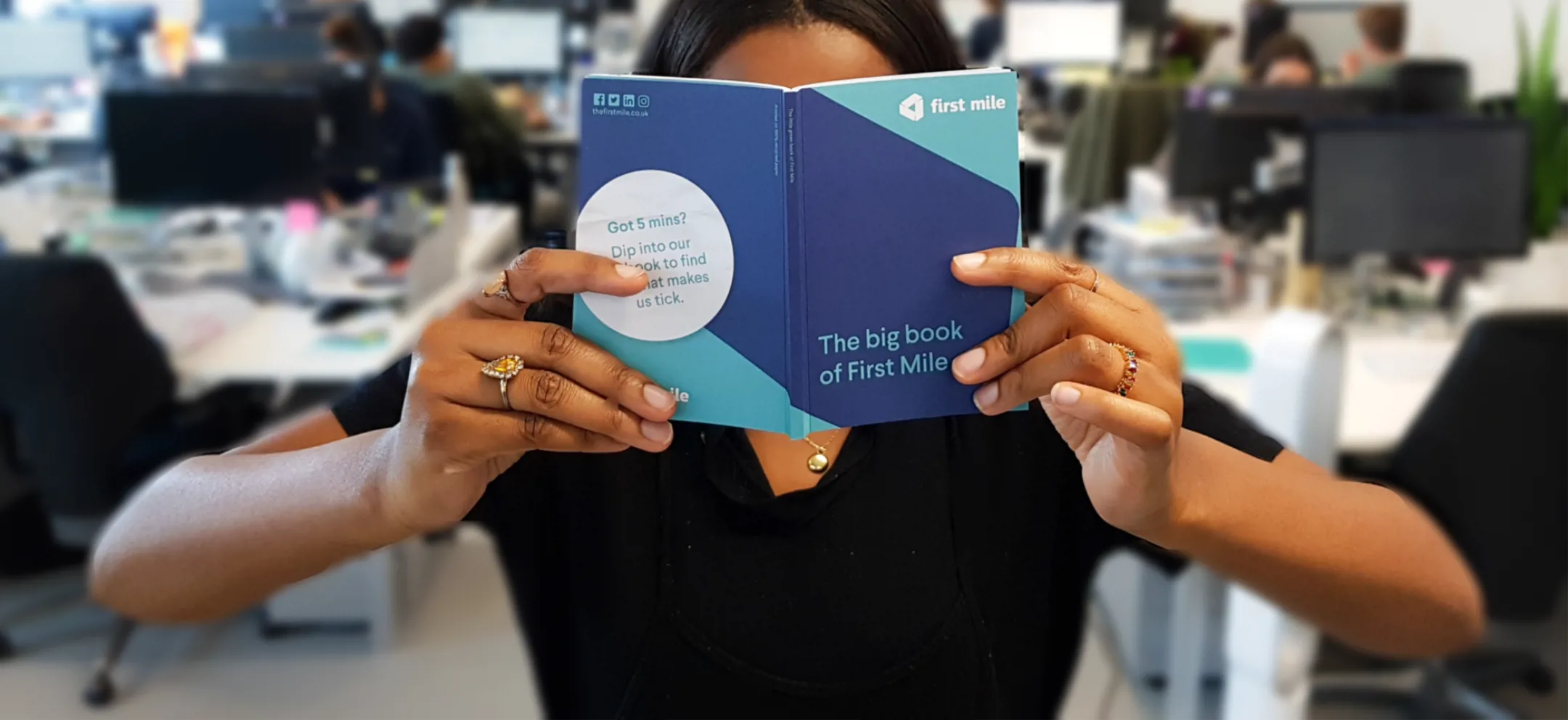 A photo of a person holding The big book of First Mile while in an office, face covered by the book