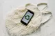 Mobile phone placed above a net bag. The recycle logo is on the mobile phone.
